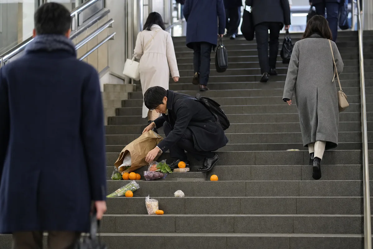 駅の階段で買い物袋の中身を落とし、拾い集めている人